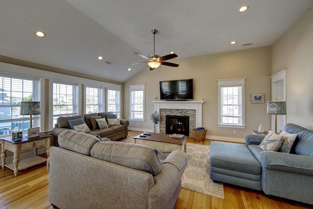 living area featuring light wood finished floors, visible vents, vaulted ceiling, a stone fireplace, and baseboards