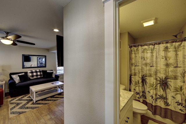 bathroom with toilet, wood finished floors, vanity, a ceiling fan, and a shower with curtain