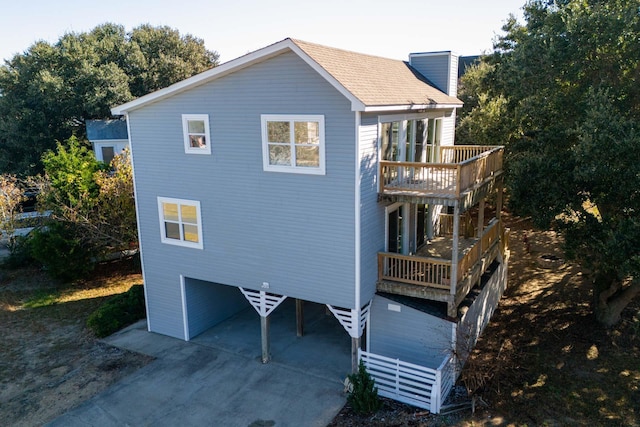 exterior space featuring roof with shingles, a chimney, a balcony, a garage, and driveway