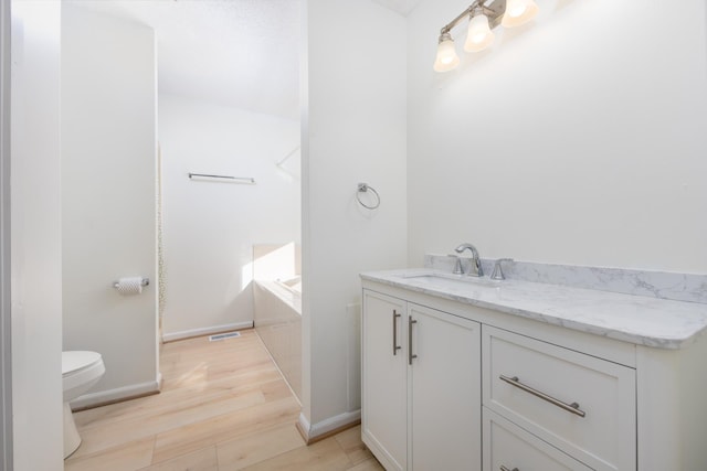 full bathroom featuring a tub to relax in, toilet, vanity, wood finished floors, and baseboards