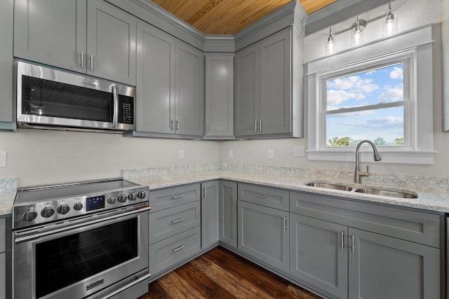 kitchen with light stone counters, dark wood-style flooring, gray cabinetry, appliances with stainless steel finishes, and a sink