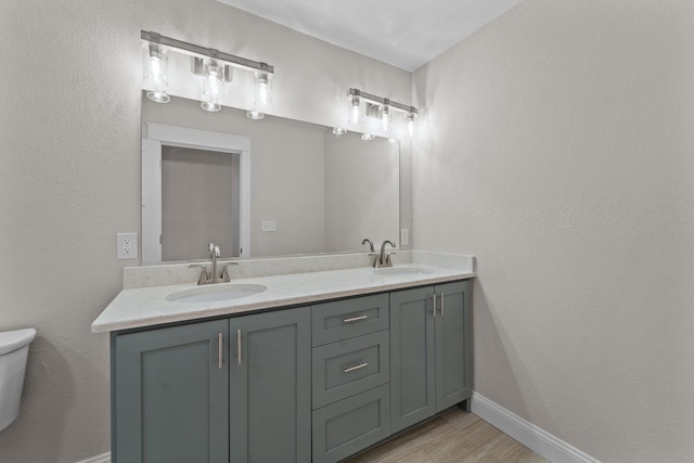 bathroom featuring toilet, double vanity, baseboards, and a sink