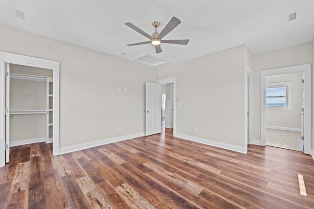 unfurnished bedroom with attic access, baseboards, dark wood-style floors, ceiling fan, and a spacious closet