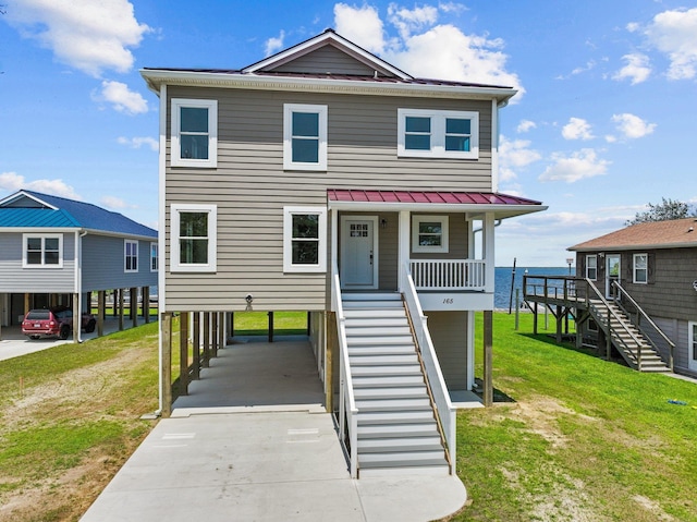 coastal inspired home featuring covered porch, a water view, a carport, driveway, and stairs