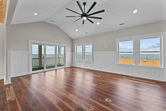 unfurnished living room featuring ceiling fan, dark wood-type flooring, a water view, vaulted ceiling, and wainscoting