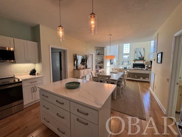 kitchen with a center island, pendant lighting, stainless steel appliances, open floor plan, and white cabinets