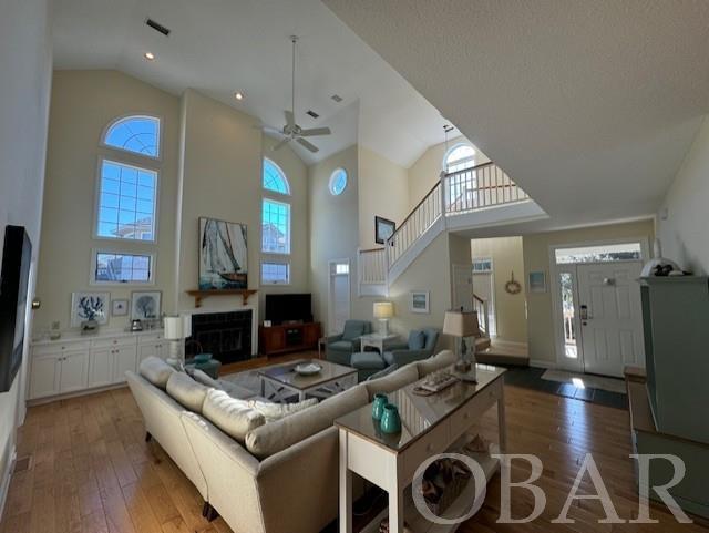 living area featuring a fireplace, dark wood finished floors, visible vents, high vaulted ceiling, and stairs