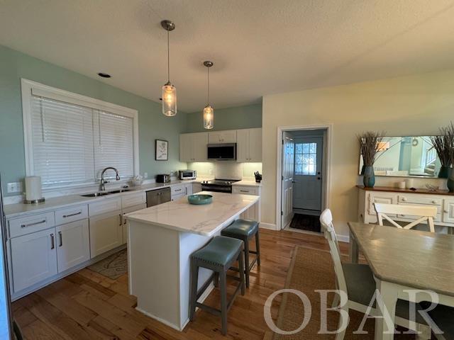 kitchen featuring appliances with stainless steel finishes, a center island, hanging light fixtures, white cabinetry, and a sink