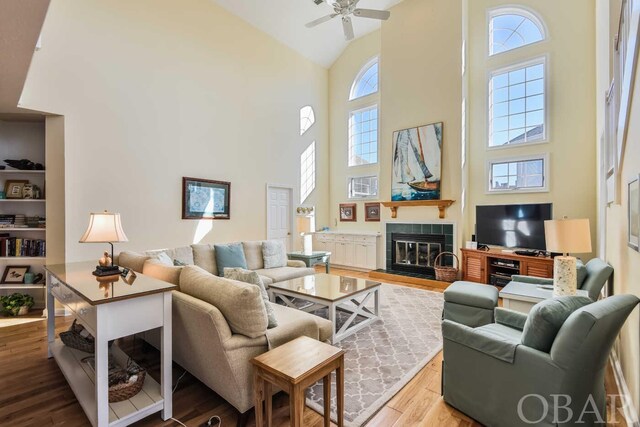 living area featuring light wood finished floors, high vaulted ceiling, a ceiling fan, and a tile fireplace