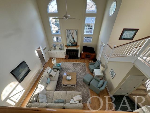 living room featuring a ceiling fan, a towering ceiling, stairway, wood finished floors, and a fireplace