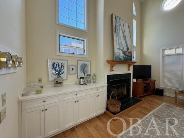 interior space featuring a towering ceiling, light wood-style floors, and a tiled fireplace