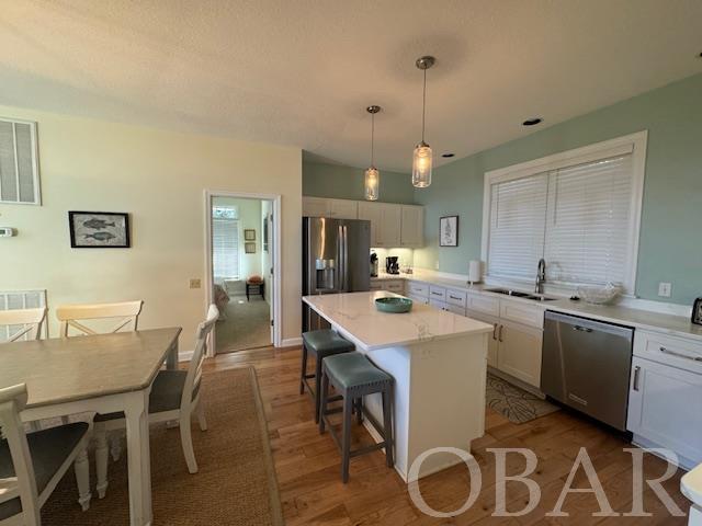 kitchen with pendant lighting, stainless steel appliances, light countertops, white cabinets, and a kitchen island