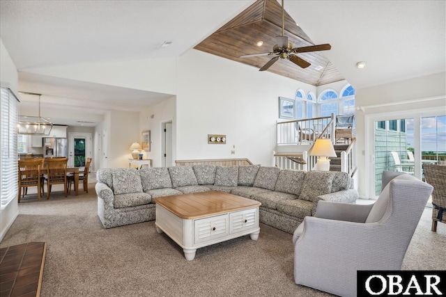 carpeted living area featuring stairway, high vaulted ceiling, and ceiling fan with notable chandelier