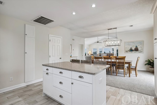 kitchen with visible vents, white cabinets, a center island, stone counters, and pendant lighting