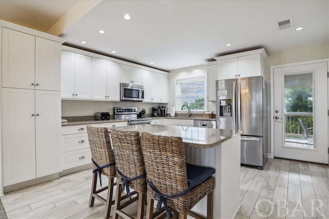 kitchen with appliances with stainless steel finishes, a center island, white cabinetry, and a breakfast bar area