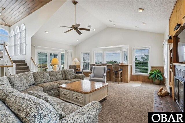 carpeted living room featuring a wainscoted wall, stairway, vaulted ceiling, and a glass covered fireplace