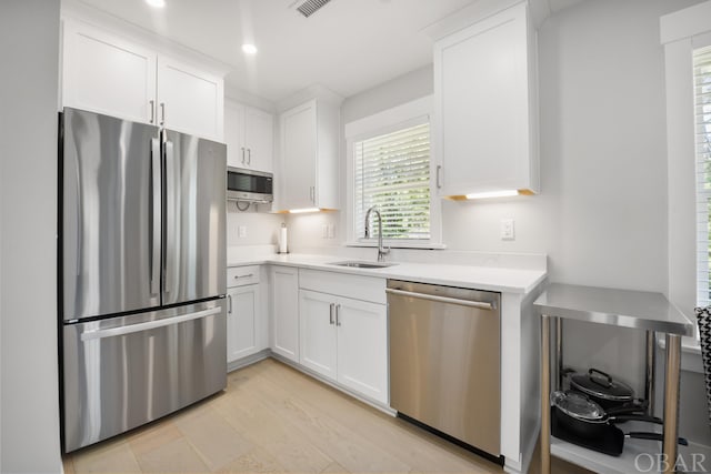 kitchen featuring white cabinets, stainless steel appliances, light countertops, a sink, and recessed lighting