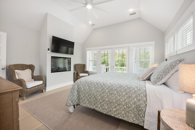 bedroom with lofted ceiling, light wood-type flooring, multiple windows, and a glass covered fireplace