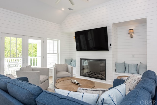 living area featuring a ceiling fan, a glass covered fireplace, vaulted ceiling, french doors, and wood walls