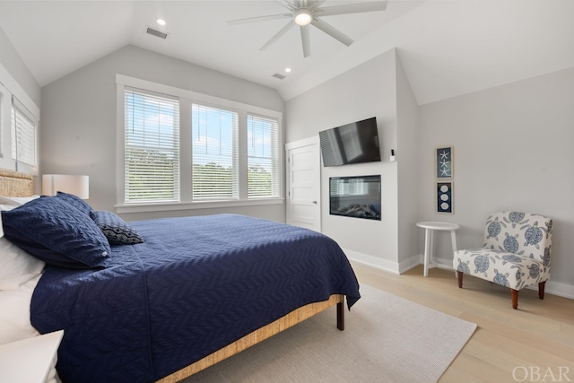 bedroom with lofted ceiling, visible vents, a glass covered fireplace, and light wood-style flooring