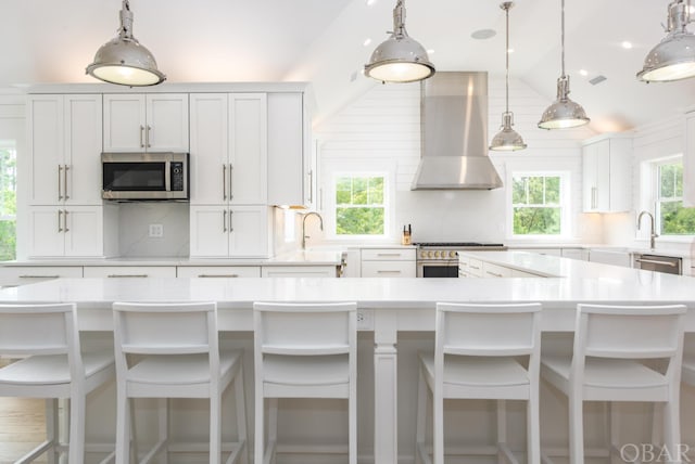 kitchen with a large island, light countertops, hanging light fixtures, appliances with stainless steel finishes, and wall chimney exhaust hood