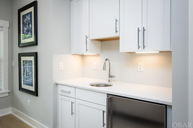 kitchen featuring baseboards, a sink, light stone countertops, and white cabinets