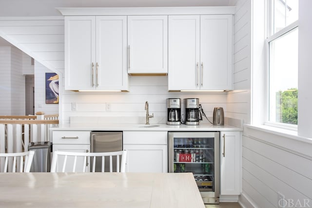 kitchen with white cabinets, wine cooler, light countertops, wood walls, and a sink