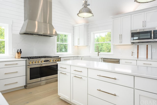 kitchen featuring stainless steel appliances, a sink, white cabinetry, light countertops, and wall chimney exhaust hood