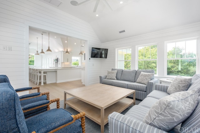 living area featuring light wood finished floors, lofted ceiling, visible vents, ceiling fan, and wood walls