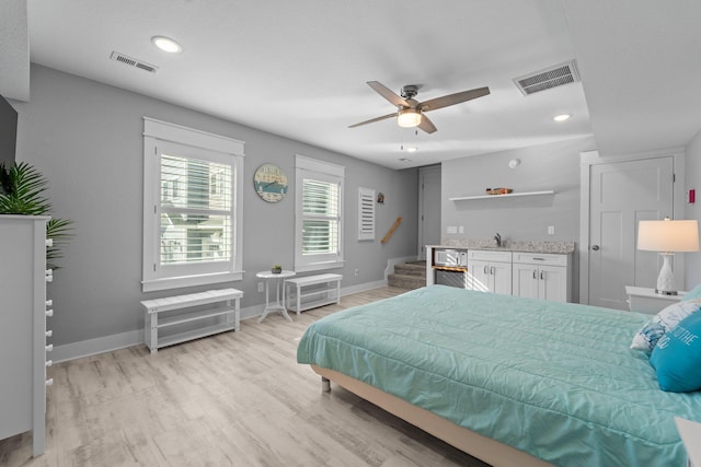 bedroom with baseboards, a sink, visible vents, and light wood-style floors