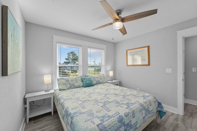 bedroom with dark wood-type flooring, a ceiling fan, and baseboards