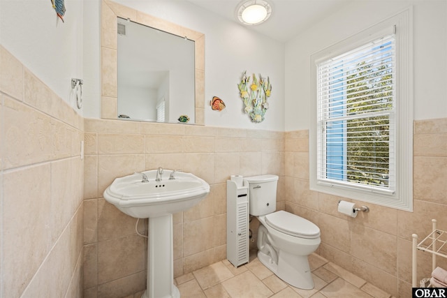 half bath with tile walls, toilet, tile patterned floors, and a sink