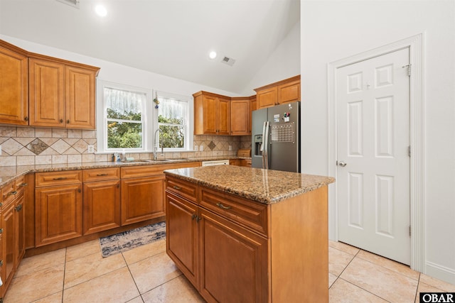 kitchen with light tile patterned floors, brown cabinets, stainless steel refrigerator with ice dispenser, and light stone countertops