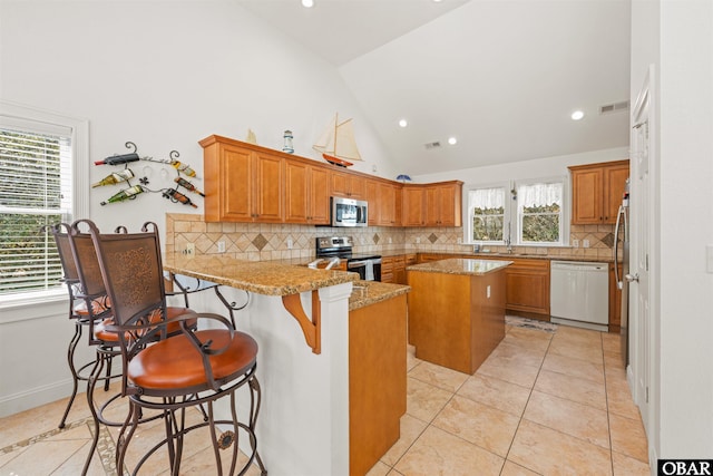 kitchen with light tile patterned floors, visible vents, a peninsula, stainless steel appliances, and brown cabinets