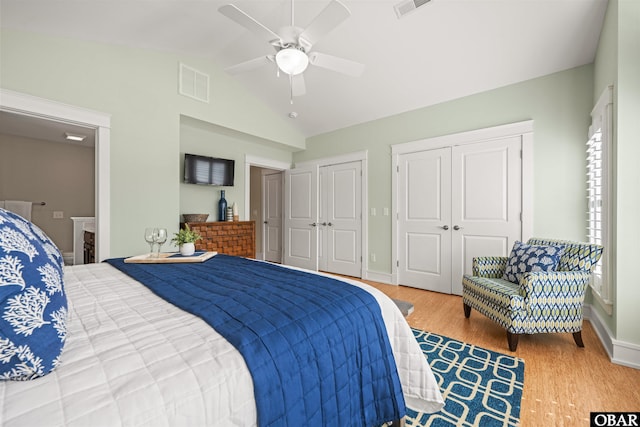 bedroom with visible vents, two closets, wood finished floors, and vaulted ceiling