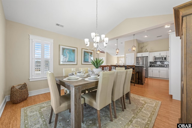 dining room featuring visible vents, baseboards, a chandelier, light wood-type flooring, and vaulted ceiling