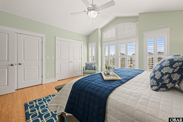 bedroom with two closets, baseboards, vaulted ceiling, wood finished floors, and a ceiling fan