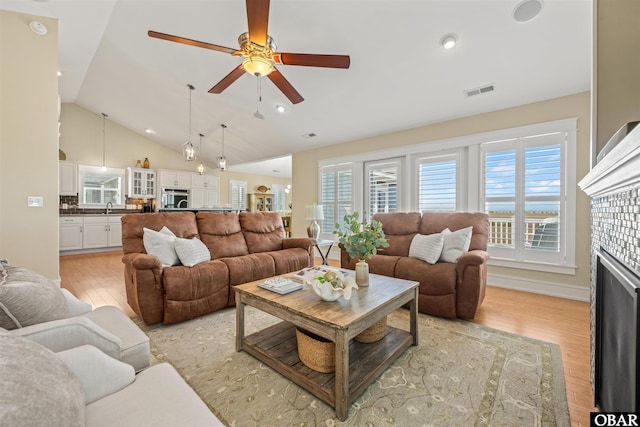 living room featuring visible vents, a fireplace, light wood-style floors, and vaulted ceiling