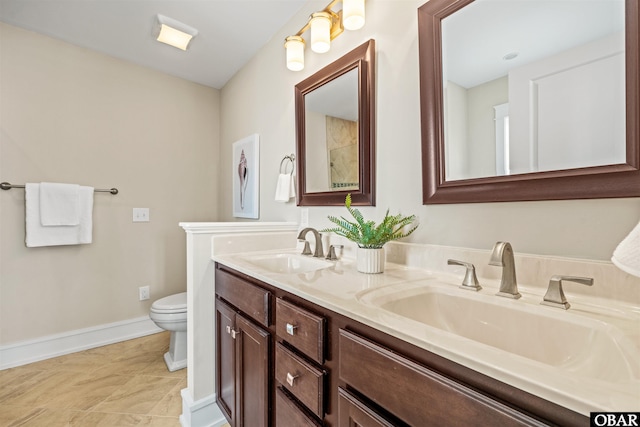 bathroom featuring double vanity, toilet, baseboards, and a sink