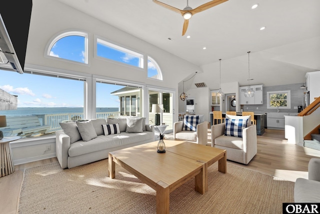 living room with stairs, a water view, light wood-style flooring, and a healthy amount of sunlight