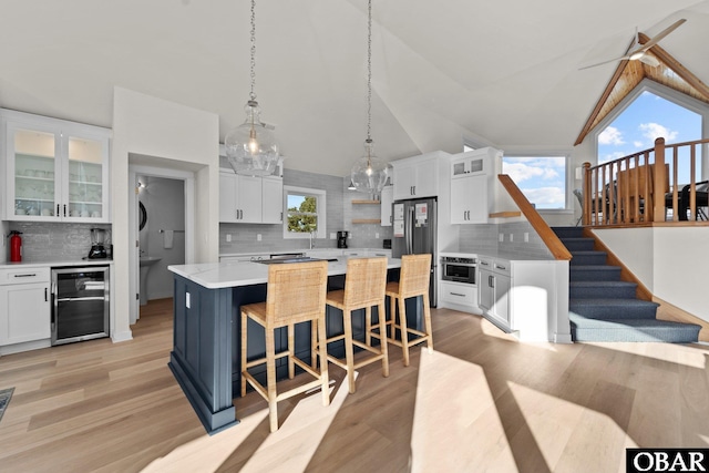 kitchen featuring wine cooler, white cabinets, light countertops, a center island, and glass insert cabinets