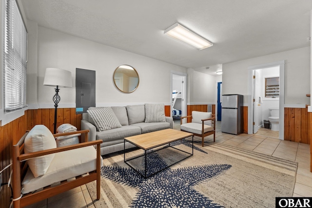 living room with wood walls, electric panel, light tile patterned flooring, and wainscoting