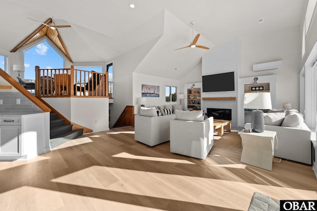 living area featuring stairway, a ceiling fan, wood finished floors, high vaulted ceiling, and a wall mounted air conditioner