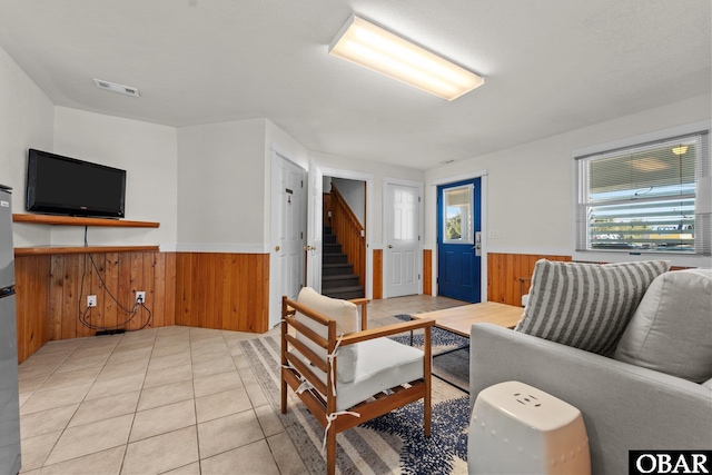 living room featuring wainscoting, wood walls, stairway, and light tile patterned floors