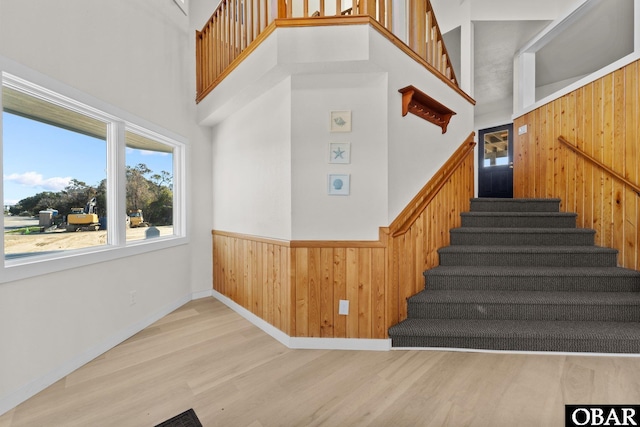 staircase with a high ceiling, wood walls, wainscoting, and wood finished floors