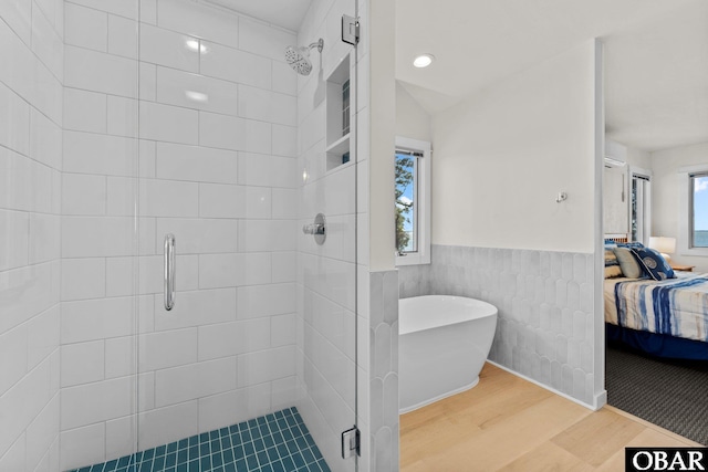 ensuite bathroom with a wainscoted wall, a stall shower, ensuite bath, wood finished floors, and a freestanding tub