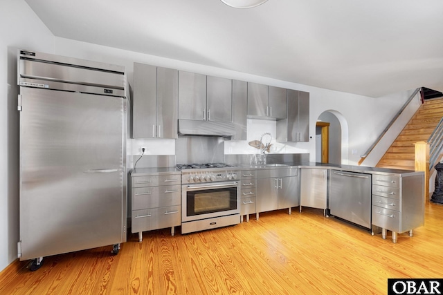 kitchen with light wood-style flooring, appliances with stainless steel finishes, gray cabinetry, under cabinet range hood, and stainless steel counters