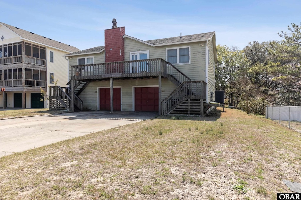 rear view of property featuring stairway, fence, an attached garage, a chimney, and concrete driveway