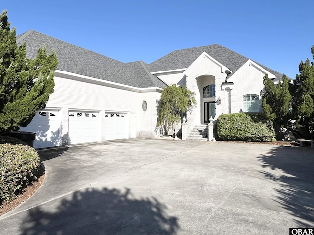 view of front of home with brick siding, concrete driveway, an attached garage, and roof with shingles