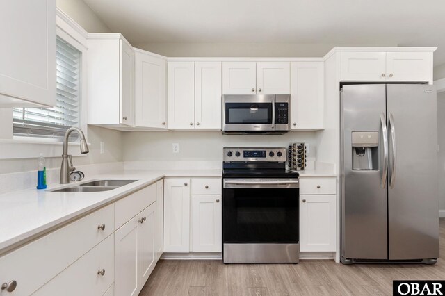 kitchen with light wood-style flooring, a sink, white cabinets, light countertops, and appliances with stainless steel finishes